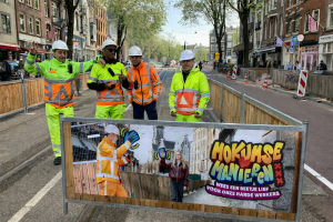 Foto van bouwhekdoek met campagne uiting met daarbij vier werkmannen