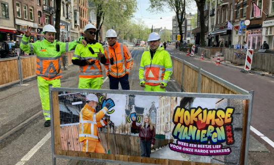 Foto van bouwhekdoek met campagne uiting met daarbij vier werkmannen
